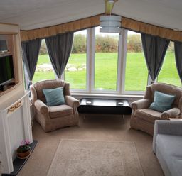 A sitting area with two armchairs and a sofa facing a low black table with large windows and curtains at Plas Tirion Caravan Llanfairynghornwy near Cemaes Bay