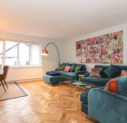 A living room with teal sofas colorful cushions glass coffee table and wall art at Tipsy Bee in Bowness-On-Windermere