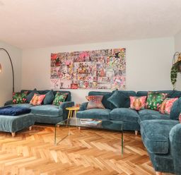 A living room with blue sofas colorful cushions glass coffee table and wall art at Tipsy Bee in Bowness-On-Windermere