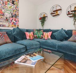 A corner sofa with colorful cushions and a glass coffee table with magazines in a living room