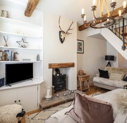A living room with a mounted deer skull above a wood stove and a television on a white built-in shelf at Glynside in Conwy