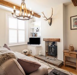 A living room with a sofa a wood stove a television and wooden beams at Glynside in Conwy