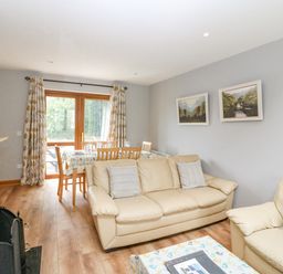 A living room with beige sofas a dining table with chairs and glass doors with curtains at 14 Sneem Leisure Village in Sneem County Kerry