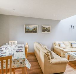 A dining area with a table set with wine glasses and a living room with two beige sofas and a wall-mounted television at 14 Sneem Leisure Village in Sneem County Kerry