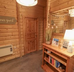 A hallway with wooden walls and door a wooden shelf with books a lamp and a mirror above at Leafy Hollow Lodge in Louth