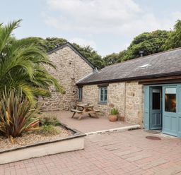 An outdoor patio area with stone buildings blue doors picnic table and plants at Pendeen in Mawnan Smith Near Falmouth