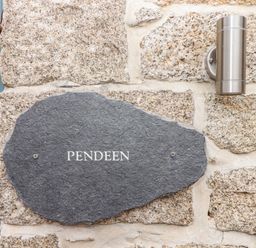 A stone wall with a black stone plaque reading Pendeen and a metal light fixture at Pendeen in Mawnan Smith Near Falmouth