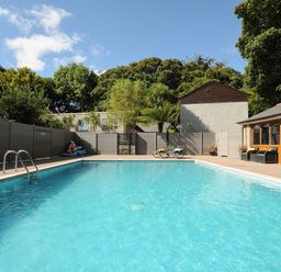 A rectangular outdoor swimming pool with a metal ladder and lounge chairs near a building at Pendeen in Mawnan Smith Near Falmouth