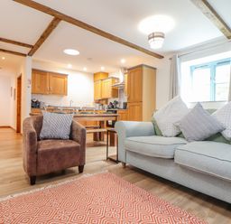 An open living room and kitchen with a gray sofa and a brown armchair at Budock in Mawnan Smith Near Falmouth