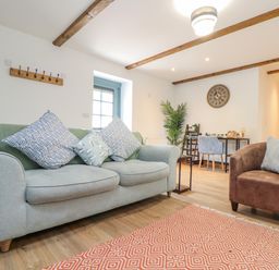 A living room with a grey sofa and brown armchair with cushions a desk and chairs in the background at Budock in Mawnan Smith Near Falmouth