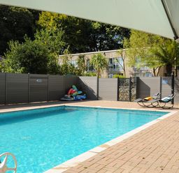 An outdoor swimming pool with blue water surrounded by a brick patio with two lounge chairs and inflatable pool toys at Budock in Mawnan Smith Near Falmouth