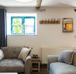 A living room with two sofas a side table a window with curtains and a wall mirror at Kerensa in Mawnan Smith Near Falmouth