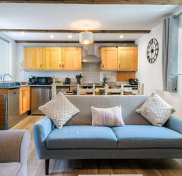 An open plan kitchen and living area with a blue two-seater sofa and wooden cabinets at Newlyn in Mawnan Smith Near Falmouth