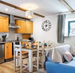 A kitchen dining area with wooden cabinets a dining table with chairs and a blue sofa by a window at Newlyn in Mawnan Smith Near Falmouth
