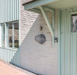 Front entrance of a building with a pale green door and window next to a textured white wall with a sign that says Porthallow at Porthallow in Mawnan Smith Near Falmouth