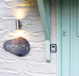 A stone wall with a light fixture and a sign that says Porthallow next to a light blue door at Porthallow in Mawnan Smith Near Falmouth