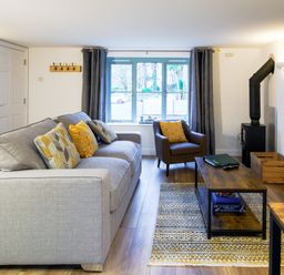 A living room with a grey sofa with pillows a brown armchair a wooden coffee table and a wall-mounted tv at Porthallow in Mawnan Smith Near Falmouth