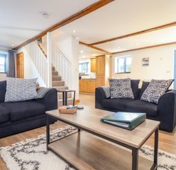 A living room with two black sofas pillows coffee table and visible kitchen area at St Keverne in Mawnan Smith Near Falmouth