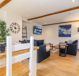 A living room with dark sofas a wall clock a floor lamp and a wall-mounted television at St Keverne in Mawnan Smith Near Falmouth