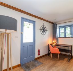 A room with a blue door wooden floor a floor lamp a desk with an orange chair and a compass wall decoration at St Keverne in Mawnan Smith Near Falmouth