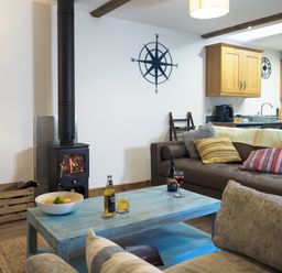 A living room with a wood-burning stove a blue coffee table and brown sofa at Manacles in Mawnan Smith Near Falmouth