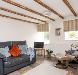 A living room with a leather sofa, armchair with footrest, small TV on a wooden table, and striped window blinds at Isfryn in Llanengan near Abersoch