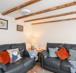 A sitting room with two black leather sofas cushions wooden beams on ceiling and a wooden side table with lamp at Isfryn in Llanengan near Abersoch