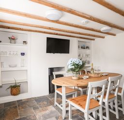 A dining room with a wooden table and chairs a television and shelves with dishes and plants at Isfryn in Llanengan near Abersoch