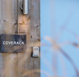 A wooden wall with a sign reading Coverack a light fixture and a combination lockbox at Coverack Mawnan Smith Near Falmouth