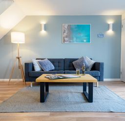 A living room with a dark blue sofa four pillows a wooden coffee table and a floor lamp at Coverack in Mawnan Smith Near Falmouth