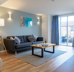 A living room with a dark sofa, coffee table, floor lamp, and sliding glass door with curtains at Coverack in Mawnan Smith Near Falmouth