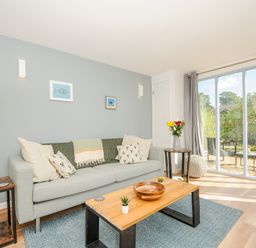 A living room with a grey sofa wooden coffee table and large sliding glass doors at Mousehole in Mawnan Smith Near Falmouth