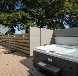 An outdoor patio with a hot tub wooden picnic table and umbrella at Mousehole in Mawnan Smith Near Falmouth