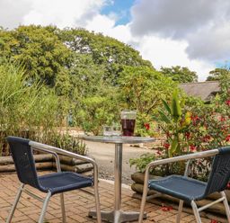An outdoor patio with a round metal table and two blue woven chairs surrounded by plants and flowers at Sennen in Mawnan Smith Near Falmouth