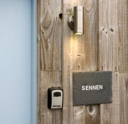 A wooden wall with a light fixture a lockbox and a sign that says SENNEN at Sennen in Mawnan Smith Near Falmouth
