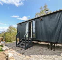 A small black corrugated metal cabin on wheels with stairs leading to open double doors and a wooden hot tub outside at Coraldie in Laggan near Newtonmore