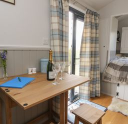 A small wooden table with a blue folder a pen a champagne bottle and two glasses next to plaid curtains and a bed at Coraldie in Laggan near Newtonmore