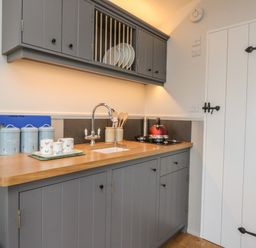 A kitchen with grey cabinets wooden countertop and a sink next to a red kettle on the stove at Coraldie in Laggan near Newtonmore