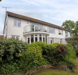A two-story white house with balconies and windows surrounded by green bushes and trees at Ynys Castell in Menai Bridge