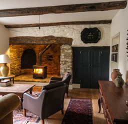 A living room with a wood burning stove in a stone fireplace chairs a wooden table a lamp and vases at Henllys Newport Pembrokeshire