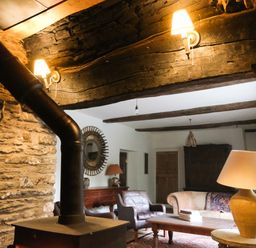 A living room with a wood stove a stone wall a beige couch a leather armchair a wooden coffee table and lamps at Henllys Newport Pembrokeshire