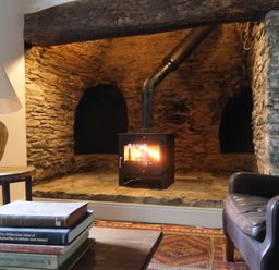 A fireplace with a burning stove in a stone hearth a brown leather chair a stack of books on a wooden table and a table lamp at Henllys Newport Pembrokeshire