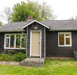 A small wooden cottage with a beige door two white framed windows a garden bench and grass at Henllys Lodge in Newport Pembrokeshire