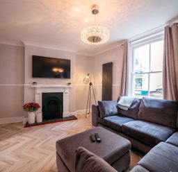 A living room with a large sofa ottoman wall mounted tv fireplace and window with curtains at Green Retreat in Dartmouth