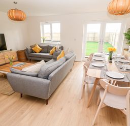 A living room and dining area with grey sofas yellow cushions wooden dining table set with plates and glasses at The Bright House in St Eval near St Columb Major
