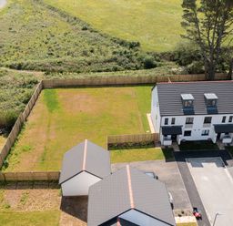 A fenced backyard with two houses and a driveway in a rural area at The Bright House in St Eval near St Columb Major