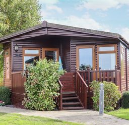 A wooden lodge with a small porch and stairs surrounded by bushes at Lodge Two Country View Park in Graveney