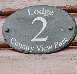 A black oval sign with white text reading Lodge 2 Country View Park on a wooden surface at Lodge Two Country View Park in Graveney