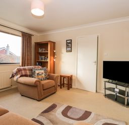 A living room with an armchair, a bookshelf, a television on a stand, and a window at Marsh Garth Kirkby-In-Furness