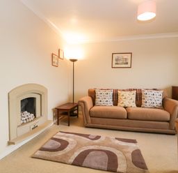 A living room with a sofa three cushions a patterned rug a fireplace a floor lamp and framed pictures at Marsh Garth in Kirkby-In-Furness